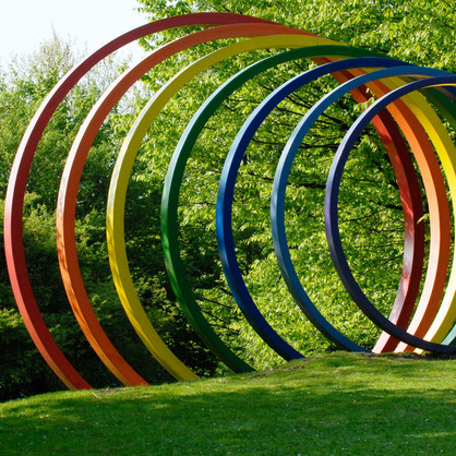 Spectral rings Large colorful steel spectral rings stand on green lawn.